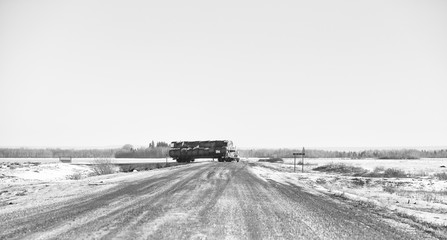 Obraz premium A semi truck and trailer loaded with round straw bales turning down a rural countryside gravel road in a black and white agricultural landscape