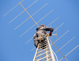 A man climbing up a steel communications tower with tools