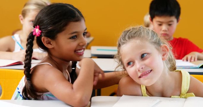 Schoolgirl whispering into her friend s ear in classroom at school 4k