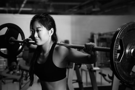 Young woman training with barbell in gym. Black and white photo