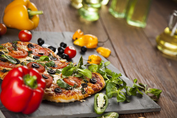 Tasty pizza, tomatoes and others ingredients on a wooden backgro