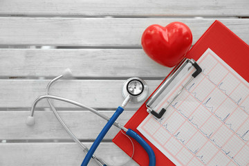 Stethoscope with red heart and paper electrocardiogram on table