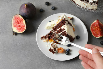 Female hand taking piece of delicious creamy cake with figs and berries on grey textured background