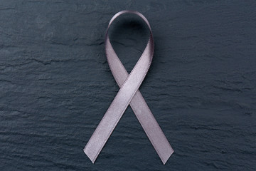 Grey ribbon on dark textured background. Brain cancer, diabetes, asthma concept