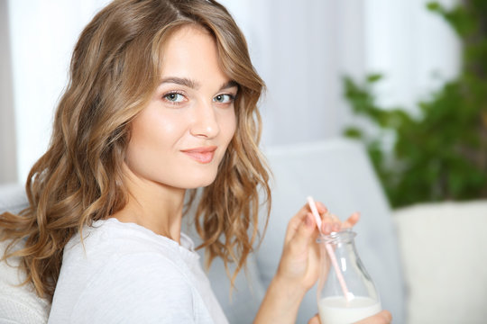 Young woman sitting on sofa with bottle of milk