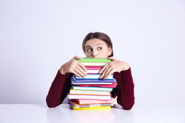 Teenage girl with pile of books sitting at table on white background