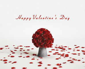 Ein Strauß mit Rosen in einer Vase und Rosenblüten auf dem Boden zum Valentinstag