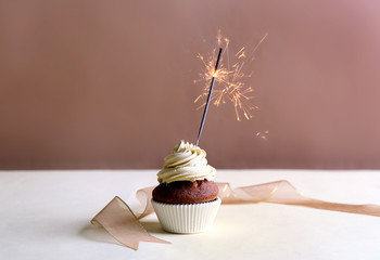 Birthday cupcake with sparkler on beige background