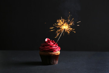 Tasty cupcake with sparkler on black background