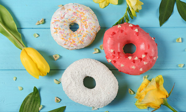 Delicious colourful donuts and flowers on blue wooden background