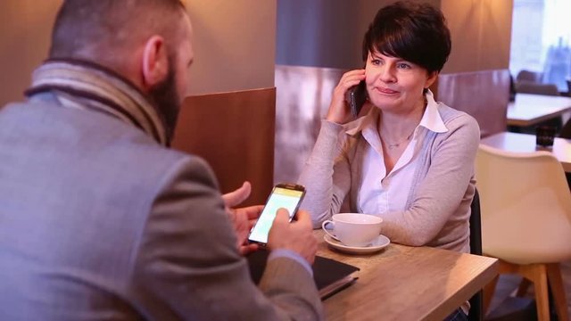 Couple businesspeople sitting in cafe with cellphone

