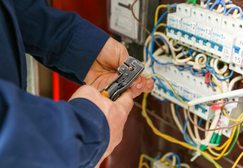Electrician stripping ends of wires in distribution board, closeup