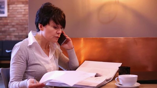 Angry businesswoman with documents talking on cellphone in caffe 
