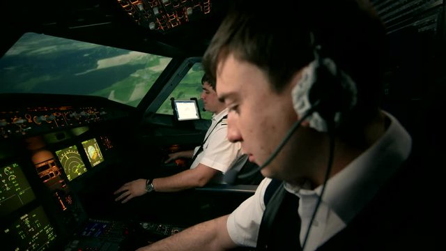 Side view of modern passenger airplane Airbus A319 A320 A321 cabin. Two professional pilots in the cockpit or flight deck of a perform turn to set the course of flight. At the background of green