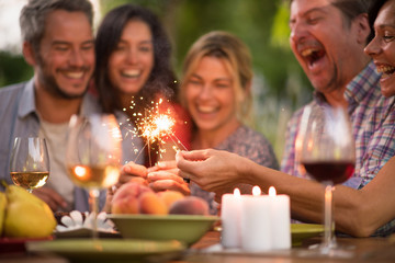 A group of friends having fun on a terrace on a summer evening, they hold spark sticks in their hands, focus on the sticks