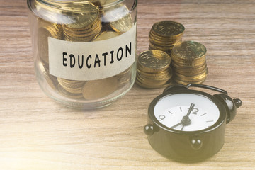 Coins in glass with EDUCATION label on wooden background. Financial concept.