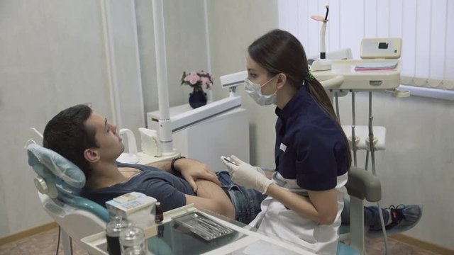 Young girl dentist making procedures with teeth male patient. Doctor treats teeth. Concept oh healthy life