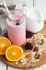 blackberry smoothie in a bottle, nuts, oatmeal, milk jug on a tray on a wooden background