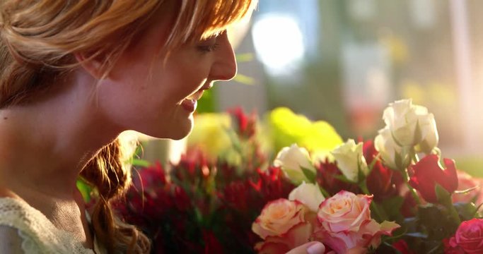 Beautiful female florist smelling pink rose in flower shop