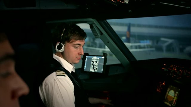 Modern civil passenger airliner or airplane at the airport apron. Knobs and dials. Panoramic shot of captain's hand. Switching of the control panel of Airbus A319 A320 A321. Airport buildings at the