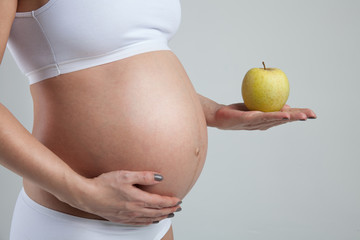 Belly of a pregnant woman with green apple on her hand