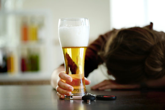 Drunk woman sitting at table with beer and car key, closeup. Don't drink and drive concept