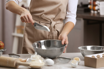 Young woman making dough in kitchen