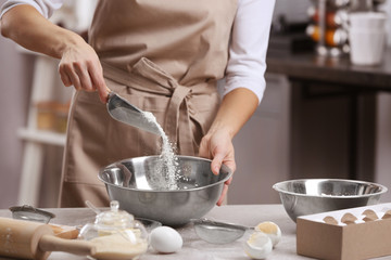 Young woman making dough in kitchen