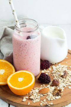 pink smoothie in a bottle with a straw, oatmeal, nuts, oranges on a white background