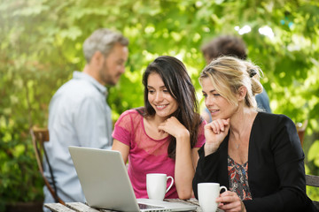 Two women friends sitting at a terrace cafe using a laptop