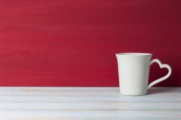 White mug with heart handle in front red grunge background.
