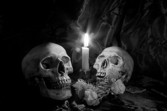 Skull with Bunch of flowers and candle light on wooden table with black background in night time in black and white/ Still life style