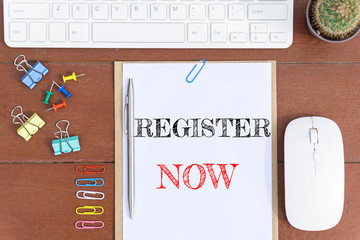 Text Register now on white paper which has keyboard mouse pen and office equipment on wood background / business concept.