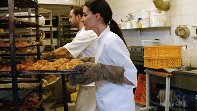 Portrait of female baker removing baked michetta from baking trolley in bakery kitchen 4k