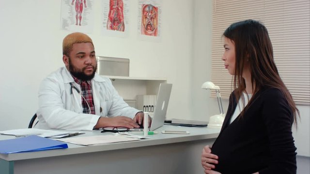 Pregnant woman visiting young smiling male doctor