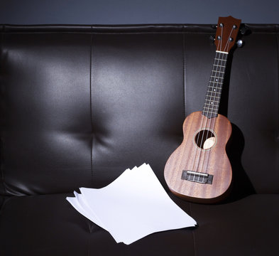 Ukulele and Blank Music Paper Notes on Brown Leather Sofa.