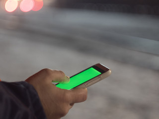 Man using smartphone with green screen at night