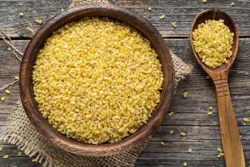 Bulgur in wooden bowl and wooden spoon over wooden background. Closeup, top view