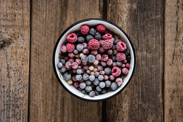 frozen berries, black currant, red currant, raspberry, blueberry in enamel bowl f on wooden table in rustic style,  top view. - 134429558