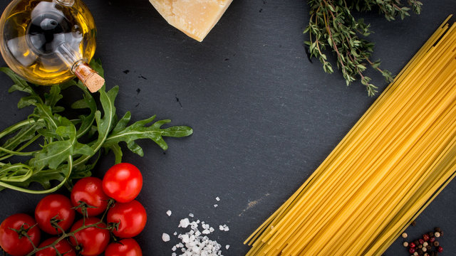 italian spaghetti, cherry tomatoes, olive oil, thyme, parmesan, arugula on black slate tray, top view, italian food concept