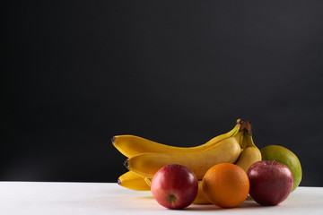 Fresh fruits: bananas, apples and orange on dark background