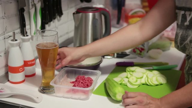 Female person cooking in the domestic kitchen and drinking beer from glass
