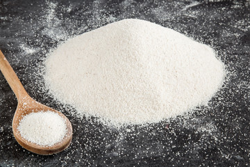 Semolina with wooden spoon on the dark background in the kitchen. Healthy eating and lifestyle.