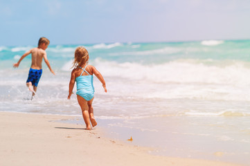 Fototapeta premium little girl and boy run play with waves on beach