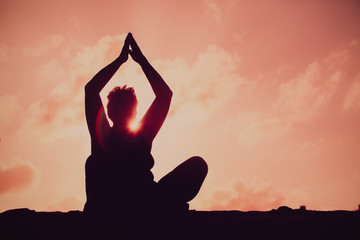silhouettes of senior woman doing yoga at sunset sky