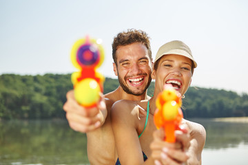 Paar mit Wasserpistolen lacht glücklich - obrazy, fototapety, plakaty
