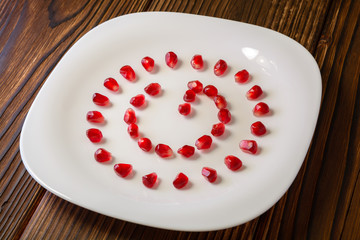 Pomegranate seeds in form of letter G on white plate on rustic w