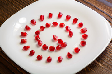 Pomegranate seeds in form of letter G on white plate on rustic w
