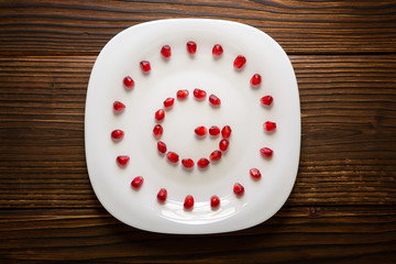 Pomegranate seeds in form of letter G on white plate on rustic w