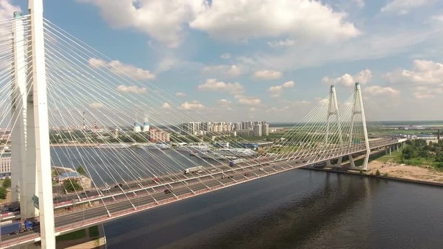 Flying along main span and white ropes of cable-stayed Bolshoy Obukhovsky Bridge. Cars driving on ring road. Aerial view. The bridge across Neva river. St. Petersburg, Russia
